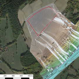 Das Bild zeigt eine Luftaufnahme einer landwirtschaftlich geprägten Landschaft mit Feldern, Waldflächen und einem kleinen Dorf am linken Rand. Über die Aufnahme ist ein farbiges Modell gelegt, das Höhenlinien und Abflusswege darstellt. Die Höhenlinien sind mit Zahlen markiert, die die Höhenmeter angeben, und die farbigen Bereiche reichen von Braun über Grün bis Blau, was unterschiedliche Höhenstufen und Wasserfließrichtungen verdeutlicht.