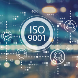 Das Bild zeigt eine grafische Darstellung mit dem Schriftzug ISO 9001 in einem großen Kreis in der Mitte. Rund um diesen Kreis sind verschiedene Symbole angeordnet, die Themen wie Qualitätssicherung, Dokumentation, Prozesse und Zertifizierung darstellen. Der Hintergrund ist unscharf und zeigt helle Lichtpunkte auf einem dunklen, bläulichen Untergrund, was der Darstellung einen modernen und technologischen Charakter verleiht.