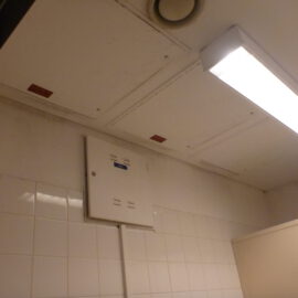 Das Bild zeigt die Decke eines Innenraums mit mehreren weißen Revisionsklappen, die in eine Zwischendecke integriert sind. An der Decke ist eine rechteckige Leuchtstofflampe sowie ein runder Lüftungsauslass zu sehen.