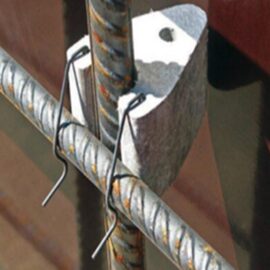 Das Bild zeigt eine Nahaufnahme von zwei gerippten Stahlbewehrungsstäben, die parallel verlaufen und durch einen Abstandshalter aus hellem Material getrennt sind. Der Abstandshalter hat eine dreieckige Form mit einer zentralen Bohrung und ist mit zwei Drahtbügeln an den Bewehrungsstäben fixiert.