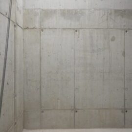 Das Bild zeigt eine glatte Betonwand mit mehreren horizontalen und vertikalen Fugen, die auf eine segmentierte Bauweise hinweisen.