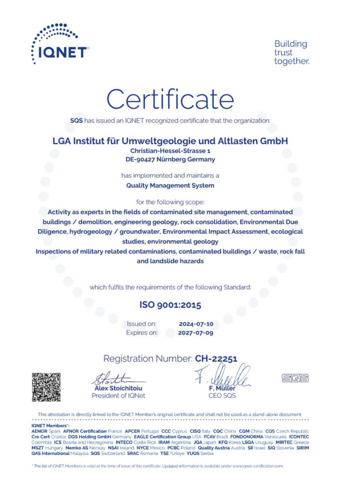 Das Bild zeigt eine englischsprachige Zertifikatsseite mit klarer, symmetrischer Gestaltung auf weißem Hintergrund. Oben sind Logo und Überschrift platziert, darunter folgen strukturierte Textblöcke zum Qualitätsmanagementsystem sowie Gültigkeitsangaben. Im unteren Bereich sind ein QR-Code, Unterschriften und weitere Prüfsymbole zu sehen.